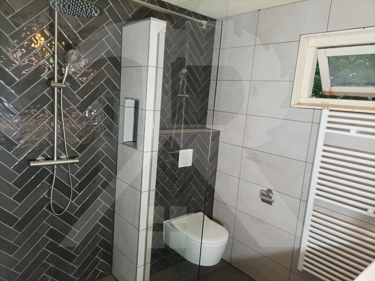 Gerenoveerde badkamer met donkere visgraattegels in de douche, een tegelnis en een hangend toilet