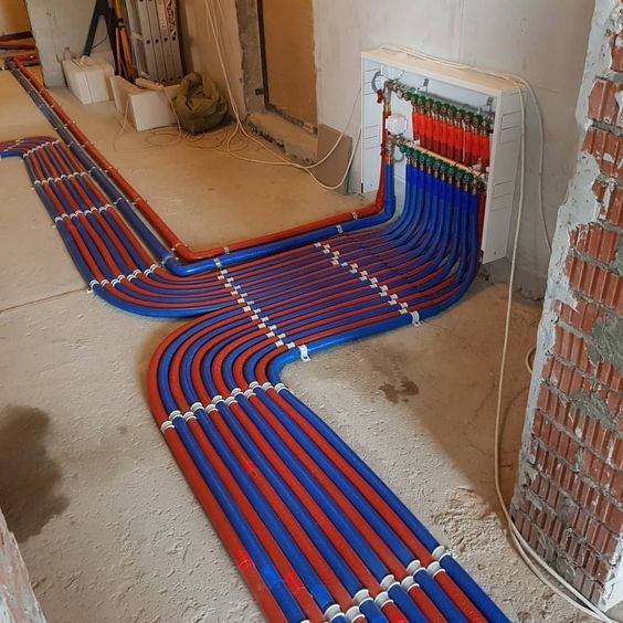 Verdeler met rode en blauwe vloerverwarmingsbuizen op een ondervloer